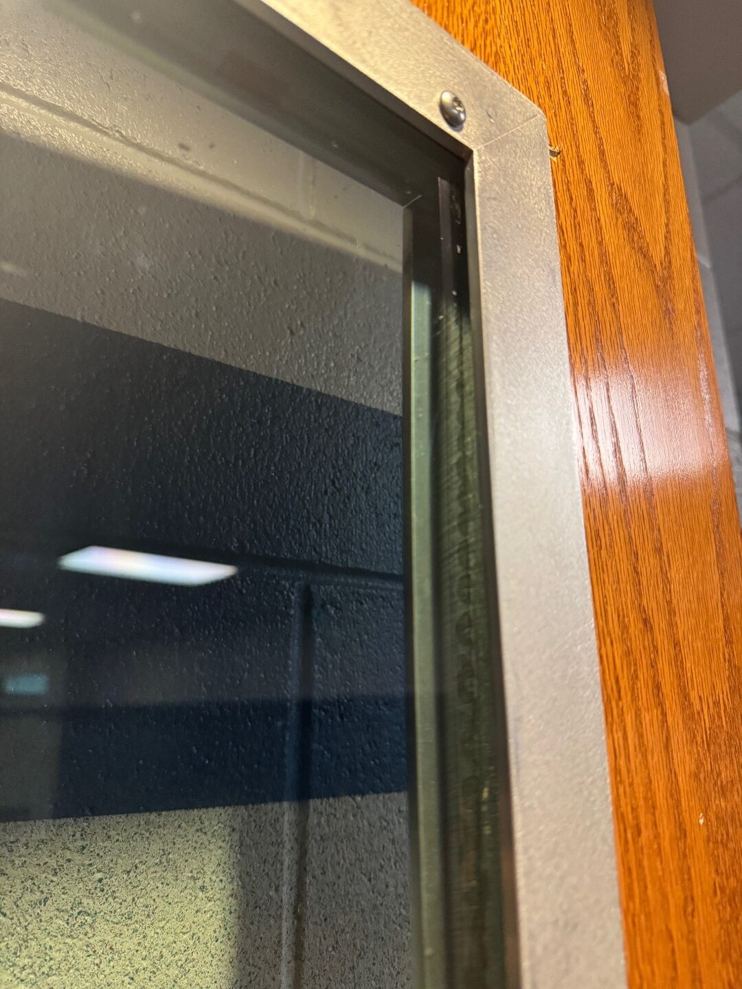 Close-up of the RetroKIT aluminum trim corner where it meets the original oak door frame. A single fastener visible at the corner of the aluminum frame.