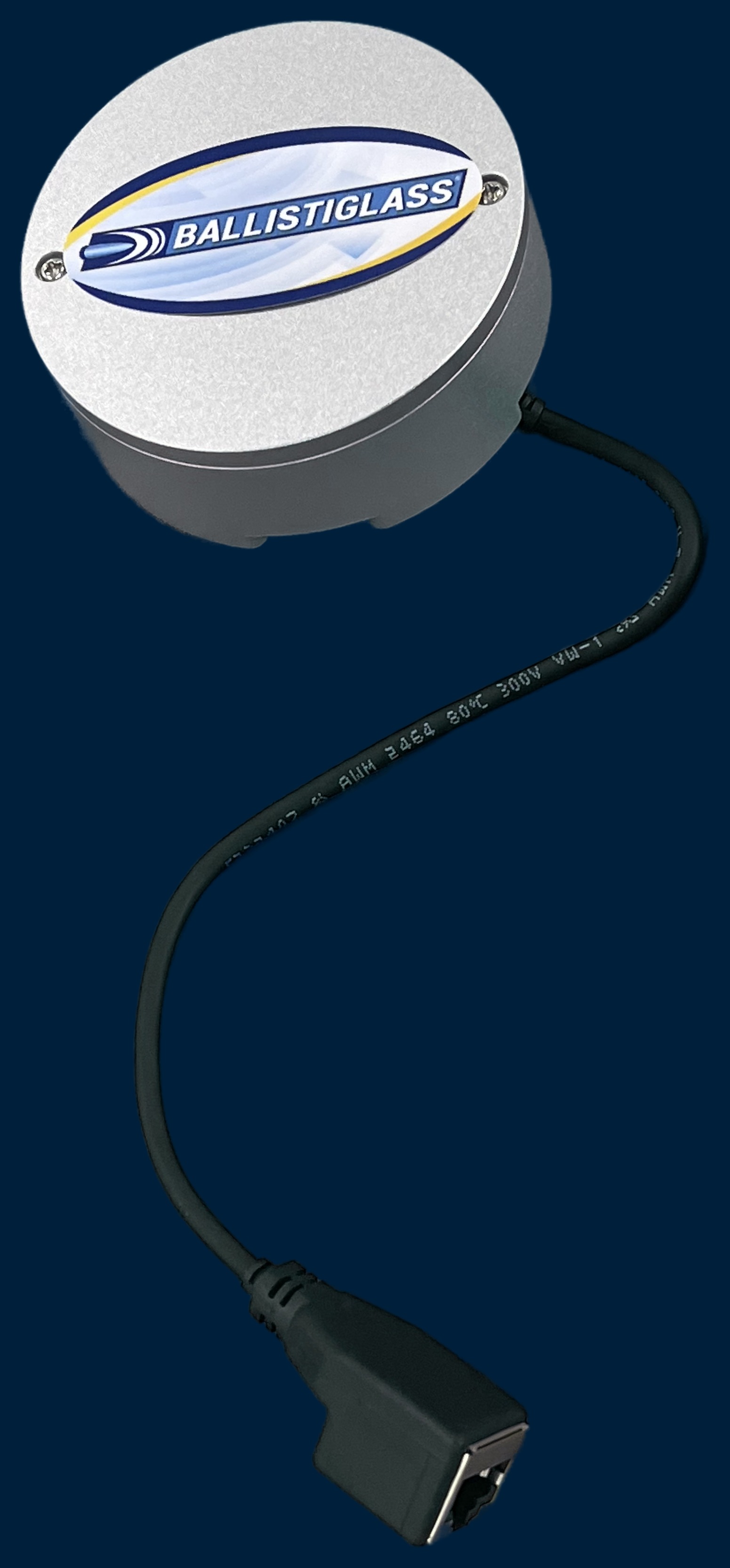 BallistiSCAN sensor — silver hockey-puck-sized disc with Ballistiglass label, a black low-voltage cable looping down to a standard RJ45 ethernet jack, photographed against a navy background as a scale reference.