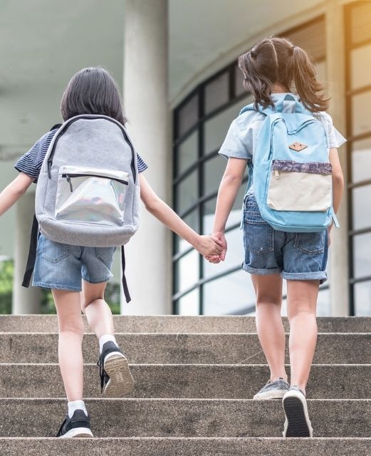 Two Schoolgirls With Bagpacks Photographed From The Back